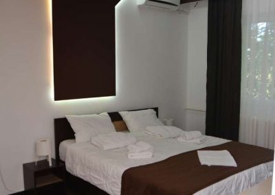 Slika bračnog kreveta sa belom posteljinom i ljubičastim pokrivačem i renoviranim zidnim svetlima